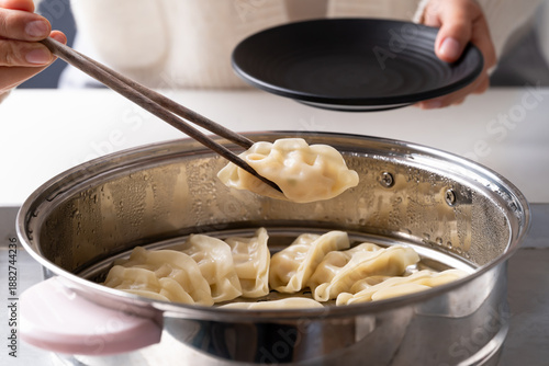 Foto Hot steamed dumpling being picked up by chopsticks from a steamer pot to a black