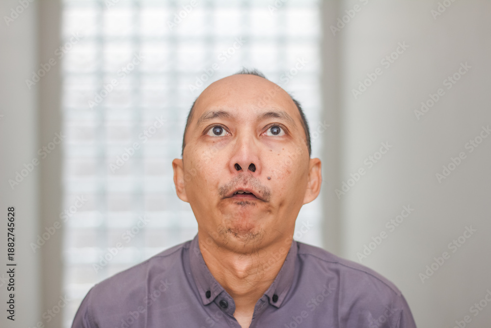 Fototapeta premium Portrait of an Asian man looking upward with a neutral thinking expression.