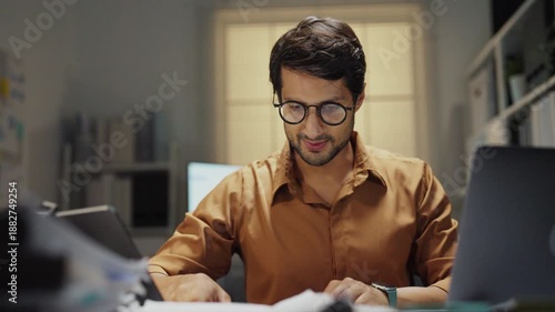 Frustrated Latin employee struggling with technology overload, facing late-night stress and working tirelessly in a dark, busy office setting.
