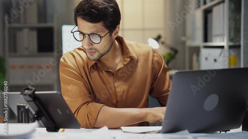 Overwhelmed Hispanic worker dealing with pressure and a heavy workload, staying late at the office to complete reports and projects amidst stress and fatigue.
