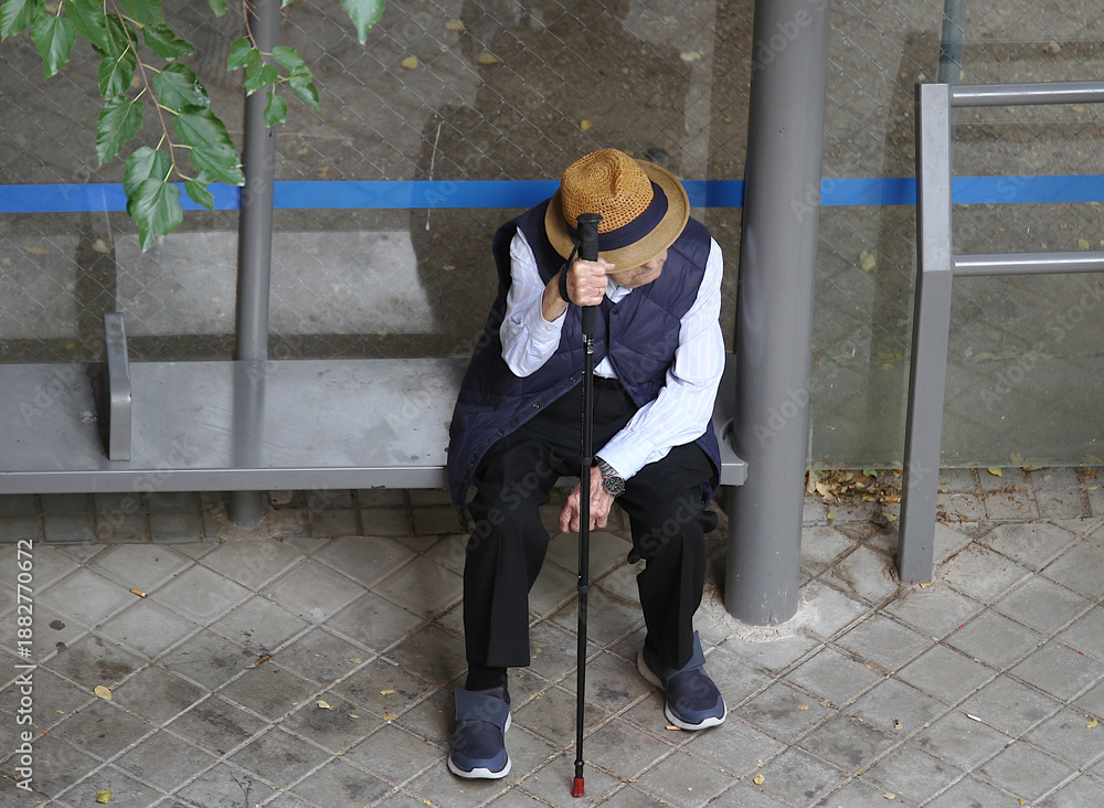 Naklejka premium abuelo viejo con bastón y sombrero esperando sentado en parada de bus al autobús