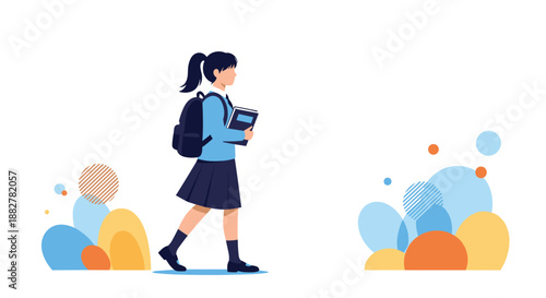 Young schoolgirl in a blue and navy uniform walking with a backpack on her shoulders and holding a book against a white background.