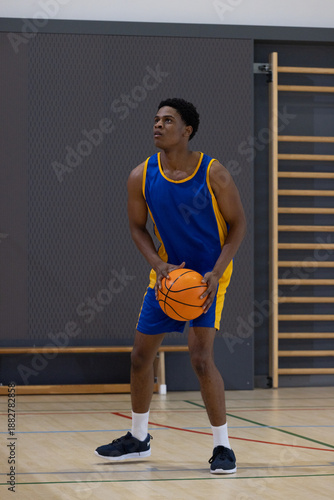 Basketball player is holding orange ball and gazing upward on wooden court near padded wall