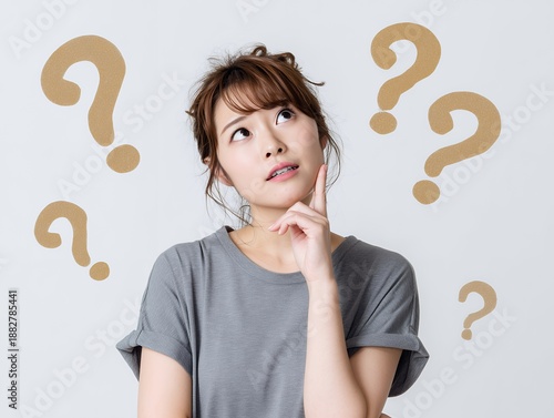 疑問符に囲まれ考え込む表情を見せる若い女性の悩みシーン