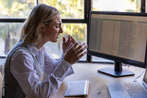 Bild auf Leinwand Woman sitting at desk by window rubbing temples with keyboard, monitor nearby, c