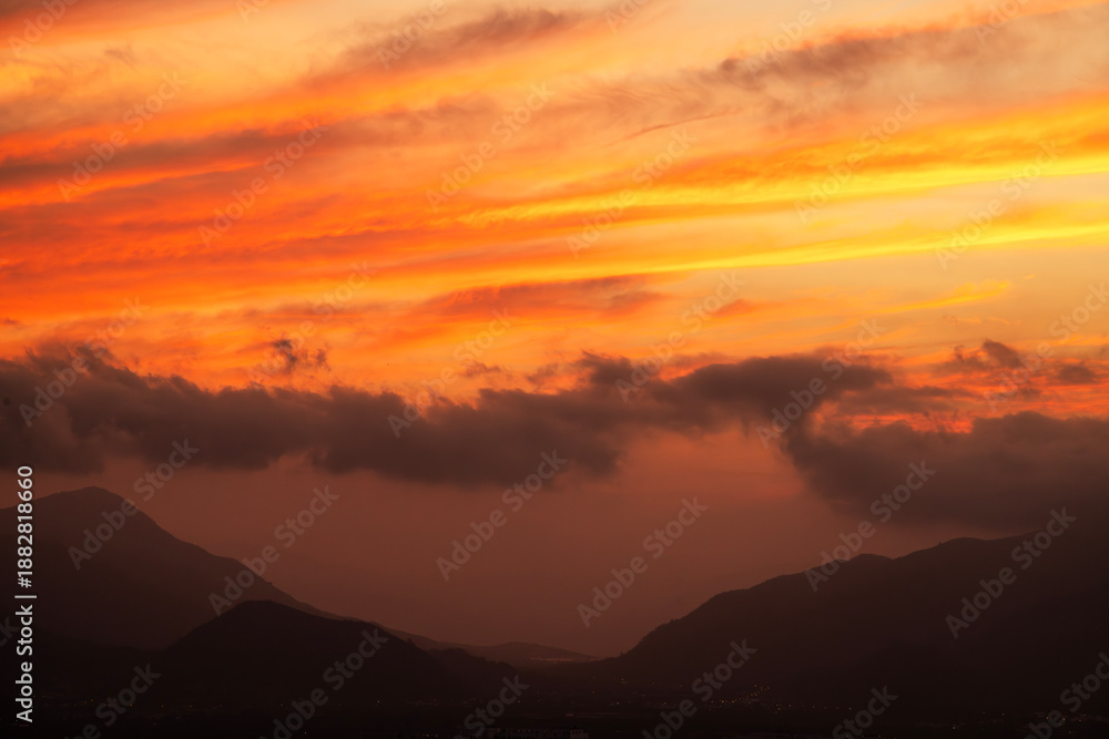 Obraz premium Beautiful bright orange sunset sky with clouds over the mountains silhouette. 