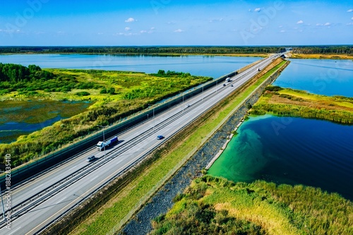 Obraz na plátne Aerial View of a Tranquil Highway with cars and trucks Bordering a Serene Lake a