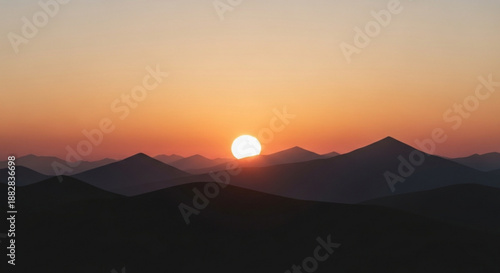 Sunset over mountain range with vibrant orange and yellow hues in the sky