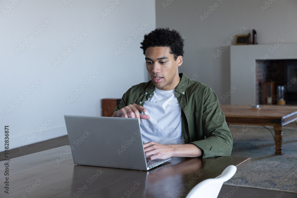 Fototapeta premium African american man typing on laptop at table gesturing toward display in living room