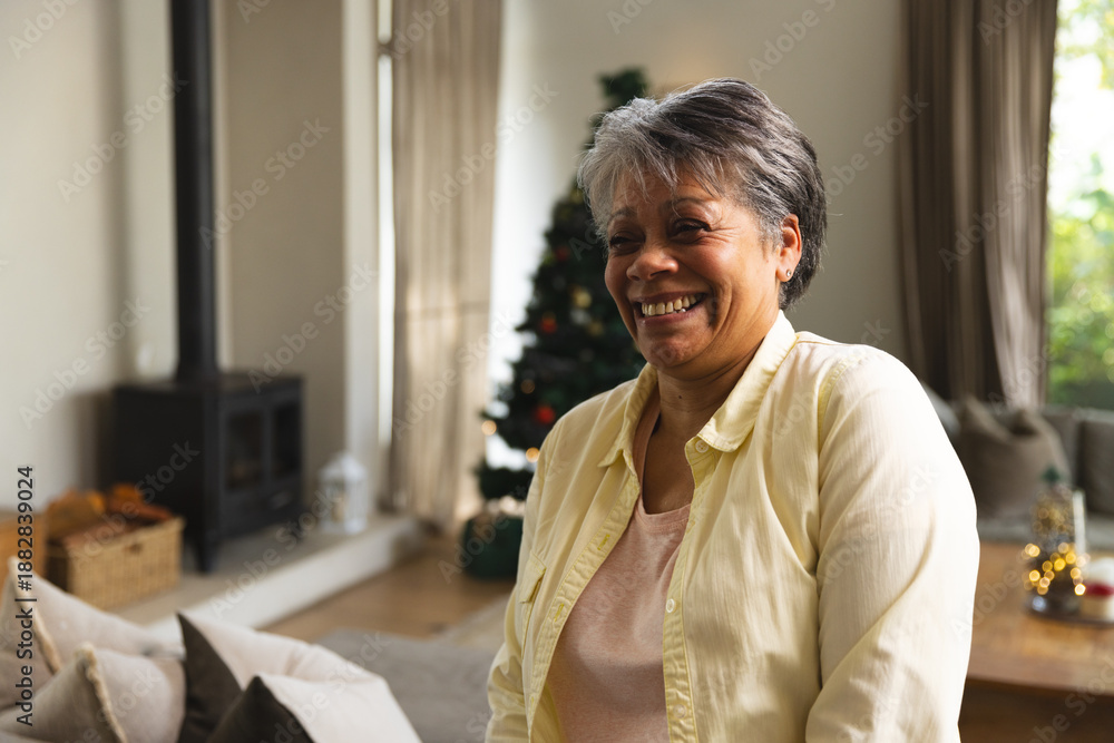 Obraz premium Senior African American woman sitting on sofa at home near decorated Christmas tree, copy space