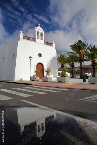 Reflection of San Isidro Labrador church in Uga, Lanzarote, Canary Islands, Spain, a traditional white church surrounded by palm trees
