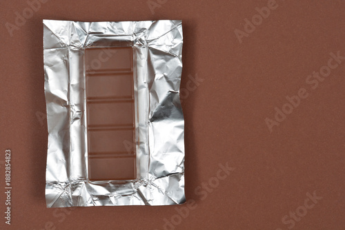 Canvas Print Milk chocolate bar placed on an open silver aluminum foil wrapper on a brown bac