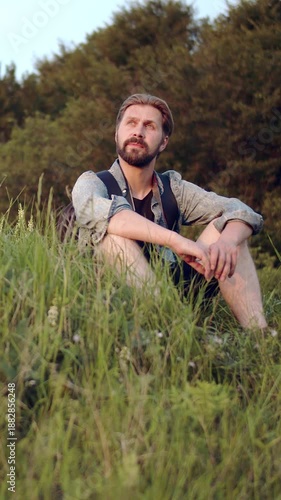 Man relaxes on grass hill during sunset, enjoying the view and warm colors.