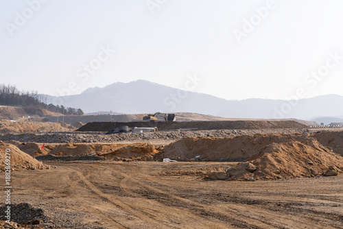 construction site with dirt road and barren land under clear sky, showing early stage infrastructure development and wide open space for future projects.