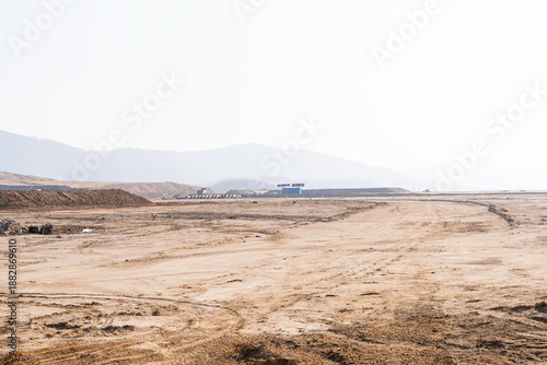 construction site with dirt road and barren land under clear sky, showing early stage infrastructure development and wide open space for future projects.