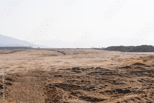 construction site with dirt road and barren land under clear sky, showing early stage infrastructure development and wide open space for future projects.