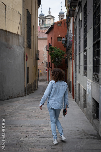 Quadro em tela Woman with curly hair exploring historic cobblestone street, seeing the pontifical basilica of st