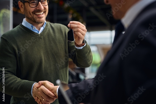 Close up of man holding new car key while shaking hands with salesperson in a showroom.