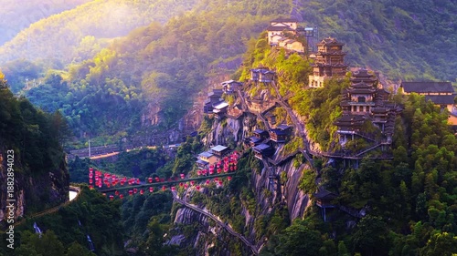 Aerial shot of traditional Chinese wooden houses built on a steep cliff in Wangxian Valley, Jiangxi, China during a golden sunset.