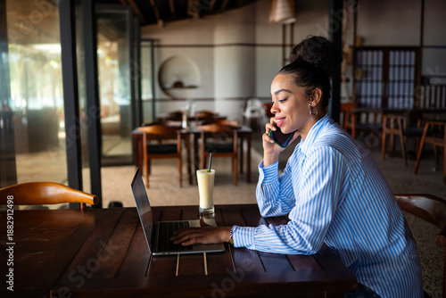 Confident young businesswoman working remotely while taking a phone call in a stylish cafe workspace