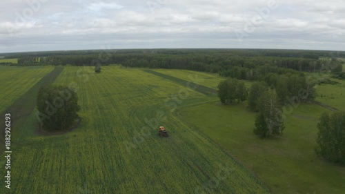Drone footage showcases the scale of agricultural land and the operation of a field sprayer against a backdrop of forest areas. The clear geometry of the fields, the movement of machinery.