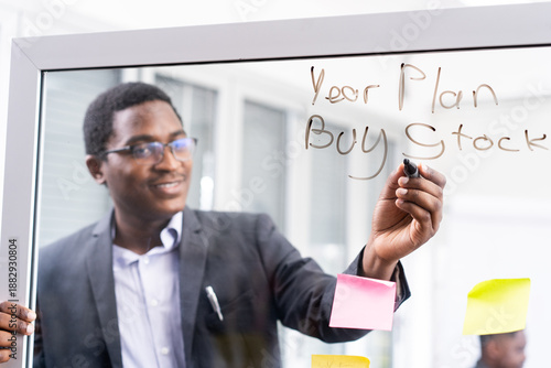 A black businessman wrote on a glass whiteboard about his year plan to buy stock.