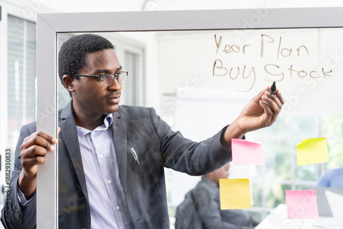 A black businessman wrote on a glass whiteboard about his year plan to buy stock.