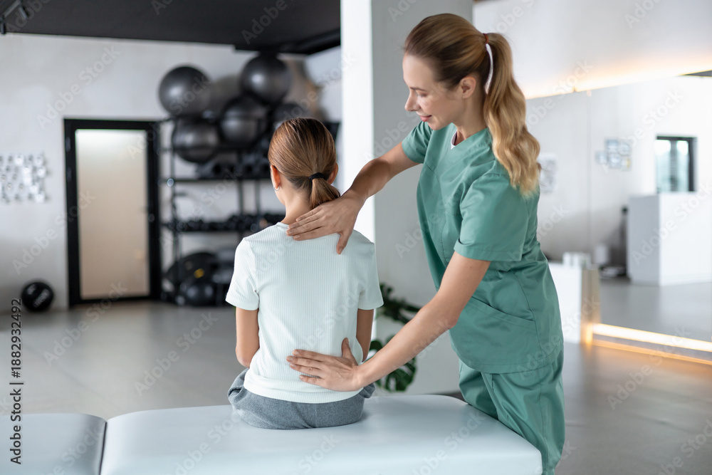 Obraz premium Woman in medical uniform guiding young girl arm mobility exercise carefully in therapy space