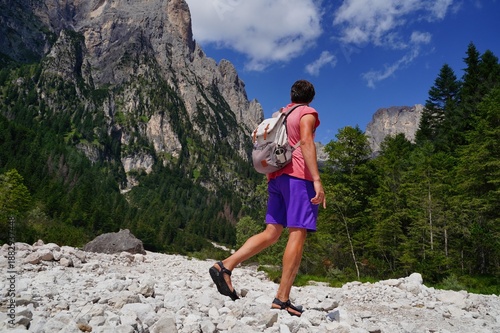 Hiker with backpack and hiking pole walking on a rocky trail surrounded by stunning mountain landscape. The scene captures outdoor adventure and exploration in nature