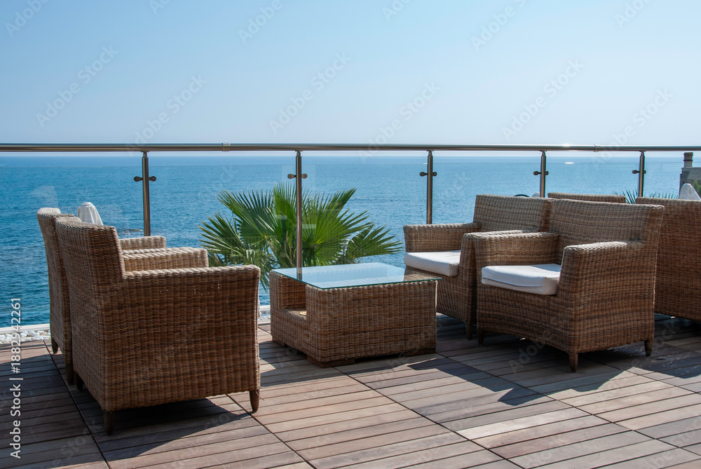 Naklejka premium Oceanfront Balcony With Wicker Seating, Glass Table, and Calm Sea View for Relaxation and Luxury Outdoor Living