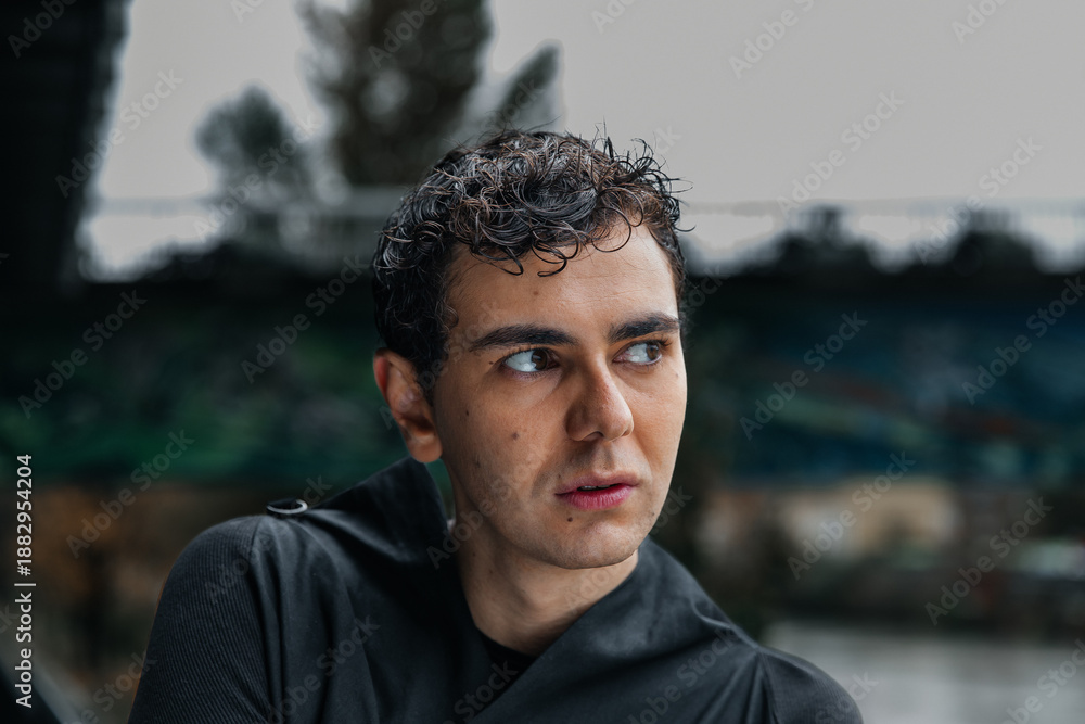 Fototapeta premium Young caucasian male with curly hair outdoors looking thoughtful