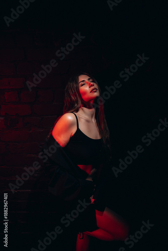 Fotografie Moody portrait of a thoughtful woman in dim red lighting against a brick background
