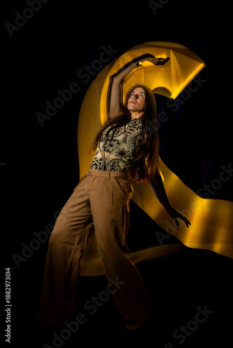 Woman creating abstract golden light painting movement in darkness