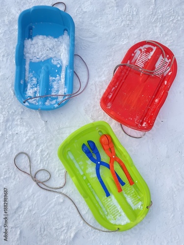 Colorful plastic sleds on snowy ground, winter outdoor toys for children.
