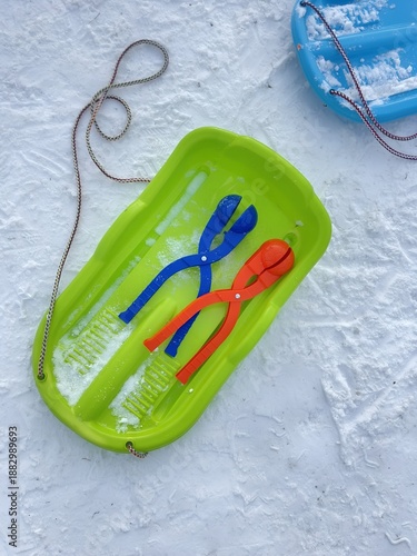 Colorful plastic sleds on snowy ground, winter outdoor toys for children.
