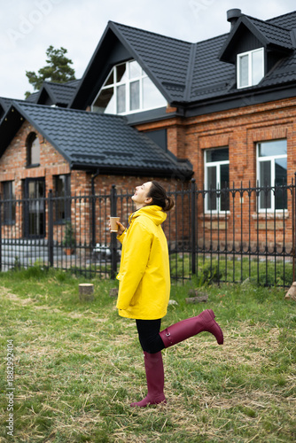 A girl in a yellow raincoat with a mug of tea in her hands is enjoying the weather.