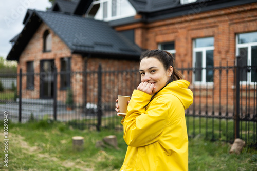 A girl in a yellow raincoat with a mug of tea in her hands is enjoying the weather.