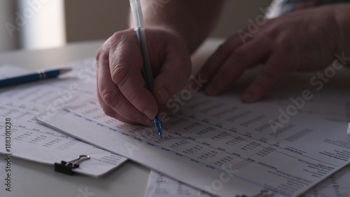 Person writing notes while reviewing documents on a table during daytime in a well-lit indoor space