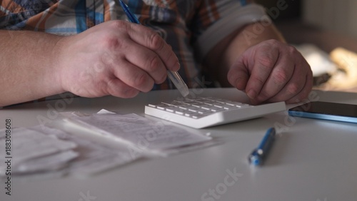 Person using a calculator while seated at a table with receipts and a phone nearby during a work session in a bright indoor setting