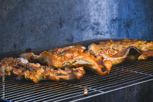 Marinated pork and pig ears grilling on a charcoal grill.