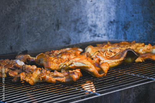 Marinated pork and pig ears grilling on a charcoal grill.