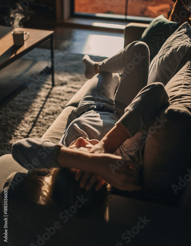 Young person relaxing on a sofa at home during golden hour with a steaming cup of coffee.