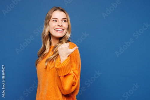 Quadro su tela Side view young happy smiling cheerful woman wear yellow sweater casual clothes point thumb finger aside indicate on area mockup isolated on plain blue background studio portrait