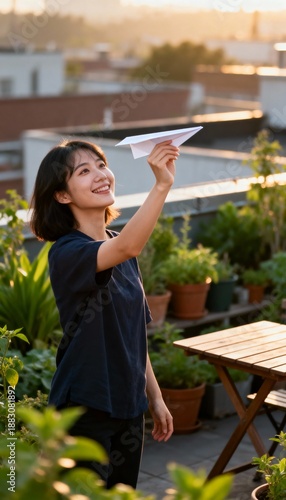 Young woman on rooftop garden launches paper airplane, sunlit, warm light