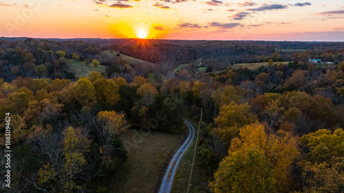 Aerial view of a winding country road cutting through autumn-kissed forests under a vibrant sunset sky, Carlisle, Kentucky, United States.