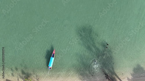 Aerial View Of A Traditional Boat With People Swimming In Turquoise Water And Sandy Shoreline