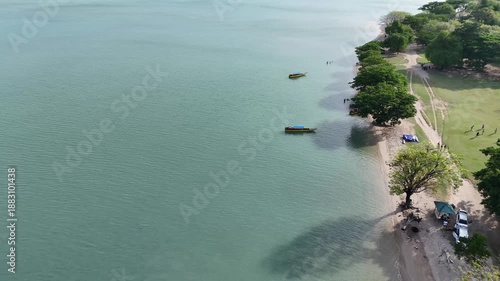 Aerial View Of Calm Turquoise Water With Small Boats And Lush Green Trees On Sandy Shoreline With People Enjoying Leisure Activities