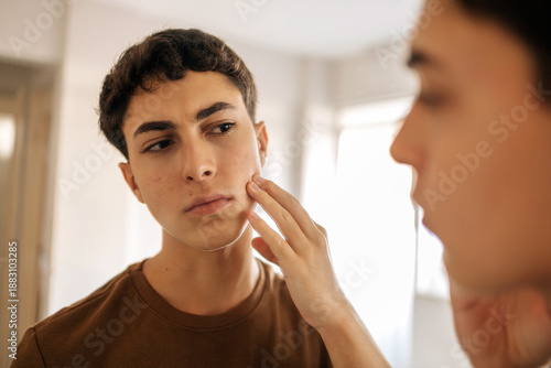 Schilderij op canvas Teenage boy looking at himself in the mirror and applying skin care product on his face