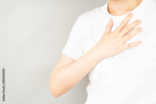 Young female suffering from chest pain over gray background. Causes of chest pain incluede angina, heart attack, GERD or costochondritis. Health care and cardiological concept. Close up.