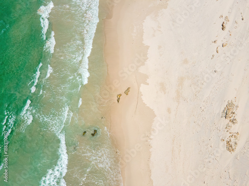 Aerial view of the sandy beach kissed by the turquoise sea, where the waves curl gently towards the shore creating a beautiful contrast of colors, Betty's Bay, Western Cape, South Africa.